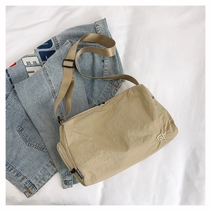 Detail of khaki nylon messenger bag with FN embroidery on a casual denim background