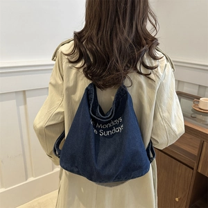 Sac fourre-tout en denim bleu marine brodé, porté sur un trench-coat beige