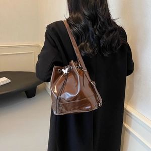 Brown high-gloss leather bucket bag with silver butterfly buckle shown on model