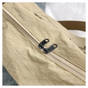 Detail of khaki nylon bag showing dual black metal zippers and wrinkled fabric texture
