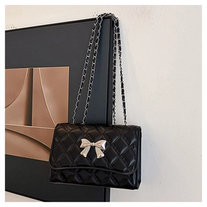 Close-up of black quilted shoulder bag featuring silver bow accent and woven chain strap