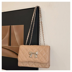 Detail view of beige quilted bag with silver bow clasp and chain shoulder strap