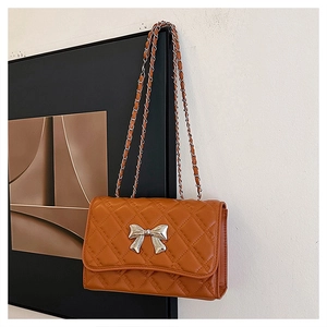 Detail of caramel quilted crossbody bag featuring a silver bow and metal chain strap