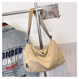 Detail view of beige nylon crossbody bag featuring wide shoulder strap and side fashion label