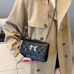 Quilted black crossbody bag with silver bow accent and chain strap worn on beige coat