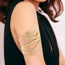 Detail of a golden coiled snake upper arm cuff with textured scales on a female model