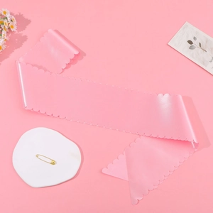 Pink satin sash detail with scalloped edges and a golden safety pin for DIY parties