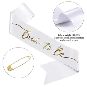 Detalle de banda Bride to Be de satén blanco con letras doradas y bordes festoneados