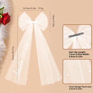 Detail of white bridal veil bow hair clip with pearl beads and 'bride to be' text