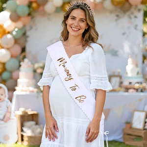 Detail of white satin Mummy To Be sash and gold headband worn by a pregnant woman