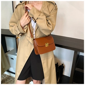 Close-up of a brown leather crossbody bag with a golden square lock on a khaki trench coat