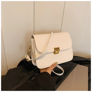 Detail of white vintage crossbody bag with gold metal clasp held by a model in casual attire