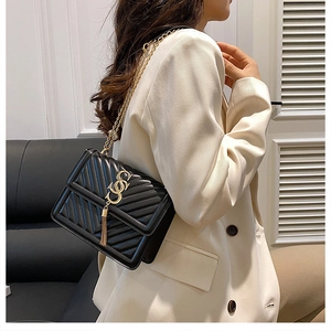 Detail of black quilted crossbody bag with gold chain strap and elegant tassel pendant