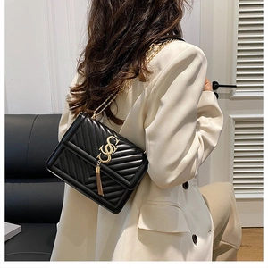 Detail of black chevron quilted crossbody bag with gold chain and metal tassel on a model