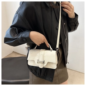 Detail of cream white textured mini bag with metal buckle and fixed top handle on model