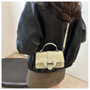 Detail of a mini light green crossbody bag with glossy wrinkled texture on leather jacket