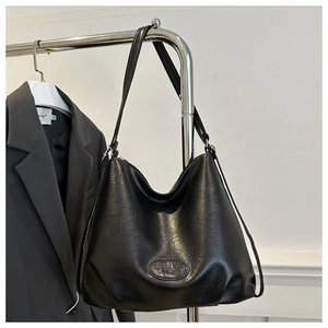 Detail of a black textured leather tote bag featuring an oval logo and slender shoulder strap