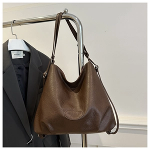 Detail of dark brown vintage faux leather tote bag hanging on a minimalist metal rack