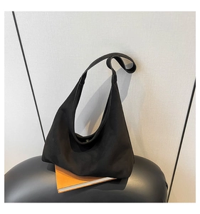 Close-up of black suede hobo bag placed on orange books with minimalist textured background