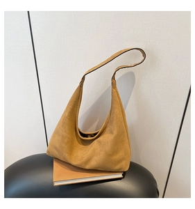 Close-up of mustard yellow suede hobo bag with magnetic snap button on a book