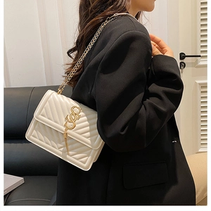 Close-up of a cream chevron quilted crossbody bag with gold chain strap on a model