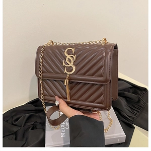 Close-up of brown quilted leather crossbody bag with golden metal logo and fringe