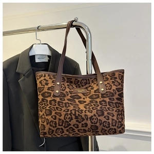 Detail of leopard print tote bag with leather straps and a metal brand plaque