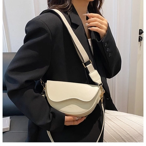 Detail of cream saddle bag featuring wave-edge flap and wide adjustable fabric strap