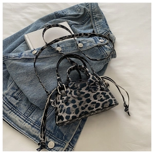 Detail view of leopard print mini crossbody bag with drawstring accents on a white bed