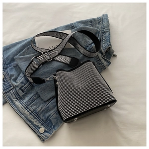 Détail du sac seau noir à strass avec bandoulière tissée sur fond de veste en jean