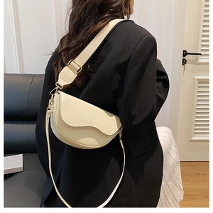 Detail of beige saddle bag with wavy flap edge and wide woven strap on a black blazer