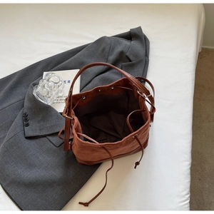 Top view of brown suede bucket bag with drawstring closure on a blazer and bed