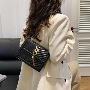 Classic black V-quilted crossbody bag with gold logo and tassel on white suit model