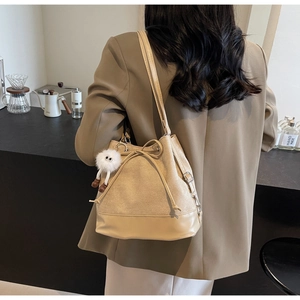 Detail of beige drawstring bucket bag featuring a white plush monster charm accessory