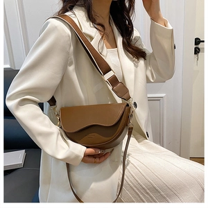 Detail of a brown saddle bag featuring contrast flap and wide canvas shoulder strap