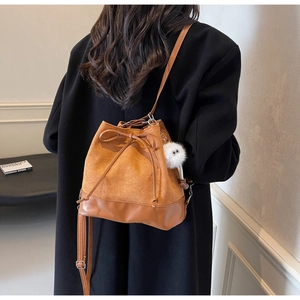 Detailed back view of a brown suede and leather bucket bag with a plush doll charm
