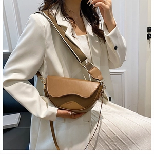 Brown leather saddle bag with wide shoulder strap worn by model in white suit