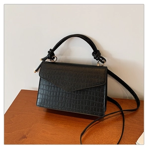 Detail der schwarzen Handtasche mit Krokodilprägung und geknotetem Griff-Design