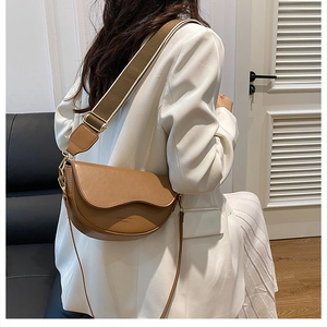 Brown leather saddle bag with wave edge flap and wide green strap on white blazer