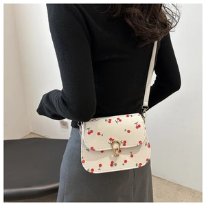 Détail du sac bandoulière blanc avec imprimé cerise et fermoir doré sur un mannequin