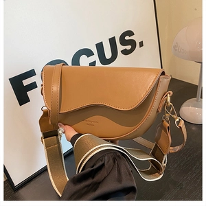 Detail of a brown leather saddle bag featuring wavy lid edge and wide fabric strap