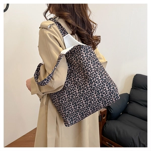 Close-up of a large leopard print canvas tote bag worn by a model in a beige trench coat