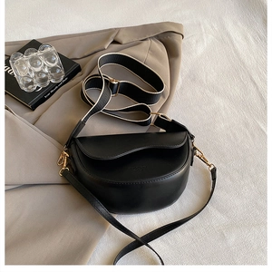 Detail of black matte leather saddle bag with wide fabric strap and embossed logo