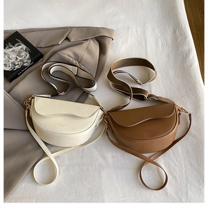 Close-up of beige and brown leather saddle bags with wavy flap and gold letter detail