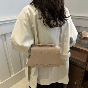 Bolso bandolera beige con diseño de alas de murciélago en una modelo con gabardina