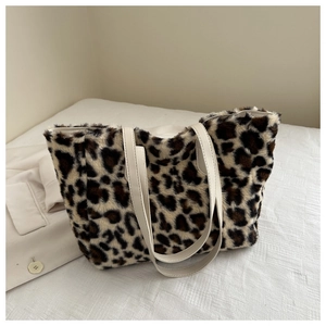 Close-up of fluffy leopard print plush tote bag with white faux leather handles on a soft fabric