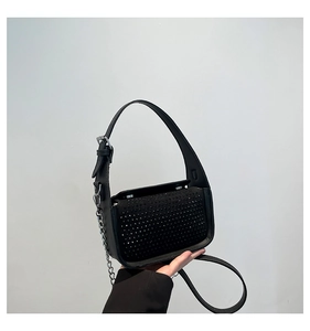 Macro detail of black handbag featuring dense rhinestone embellishments and silver chain strap