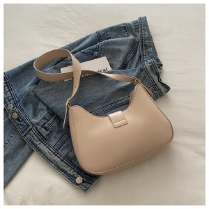 Top view of beige leather crescent bag placed on blue denim jacket for casual style
