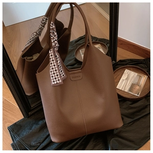 Detail of dark brown lychee leather tote bag featuring a decorative silk scarf and fashion stamp