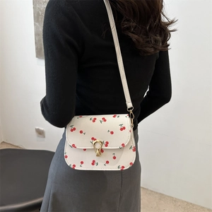 Sac bandoulière blanc à motif cerise et boucle dorée porté par un mannequin femme